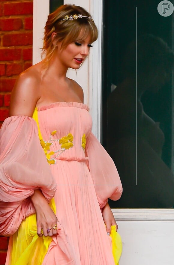 Taylor Swift em look esvoaçante segurando o vestido para andar pela rua