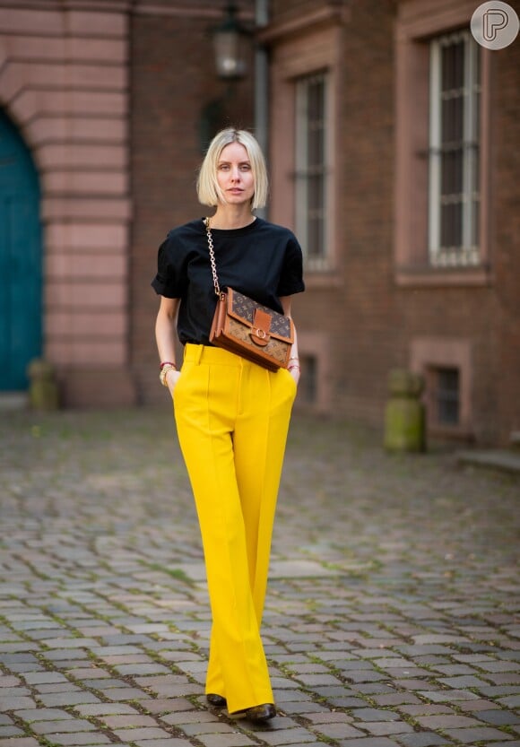 Calça pantalona amarela com t-shirt preta e bolsa de correntes