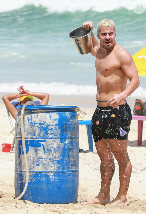 Thiago Martins se refresca ao pegar água do mar com balde na praia da Barra da Tijuca, zona oeste do Rio de Janeiro