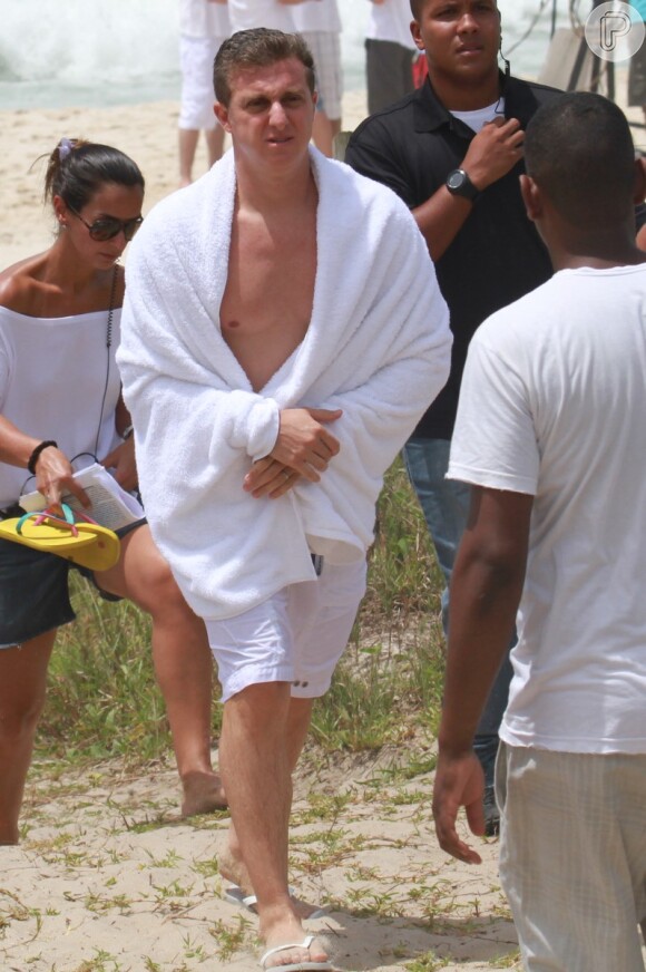O apresentador Luciano Huck sai do mar enrolado em uma toalha