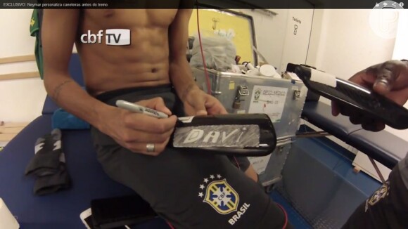 Neymar usa esparadrapos para colar o nome do filho, Davi Lucca, nas suas caneleiras. O jogador se prepara na sala de massagem