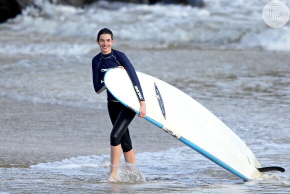 Anne Hathaway deixa o mar carregando sua prancha de surf