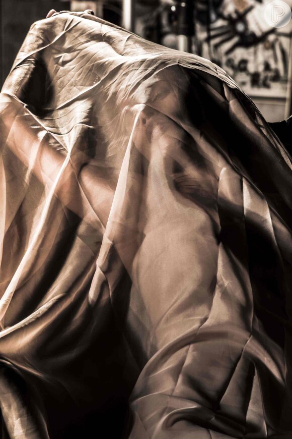 Nesta foto a nudez da modelo é levemente oculta pelo tecido transparente, no ensaio 'Sombra e Luz' de Marina (Tainá Müller), em cena da novela 'Em Família'
