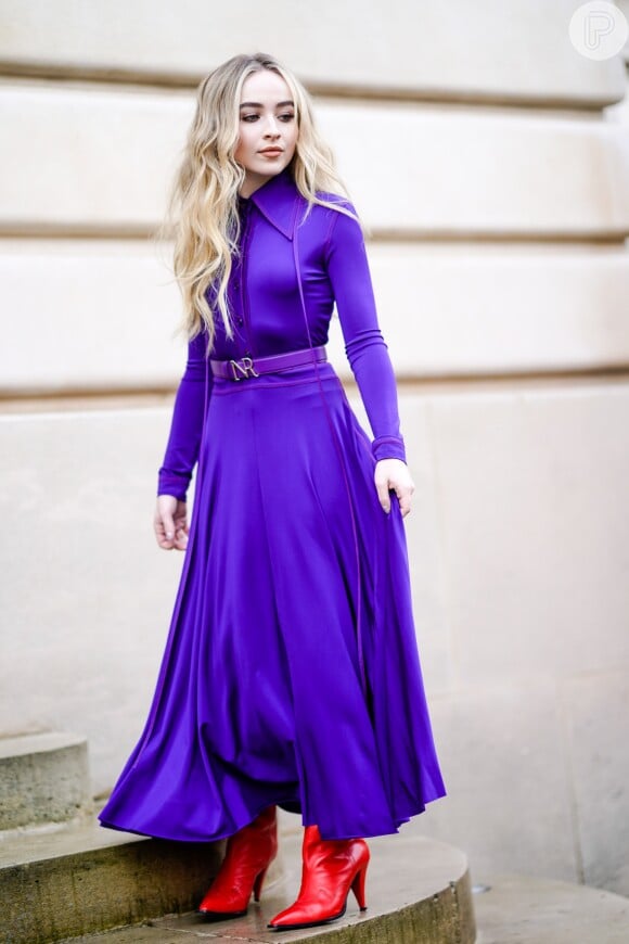 A cantora norte-americana Sabrina Carpenter contrastou o vestido roxo com as botas vermelhas para prestigiar o desfile da coleção outono/inverno 2018-2019 de Nina Ricci na Paris Fashion Week, na França, em 2 de março de 2018