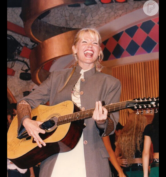Xuxa, com os cabelos presos, toca violão
