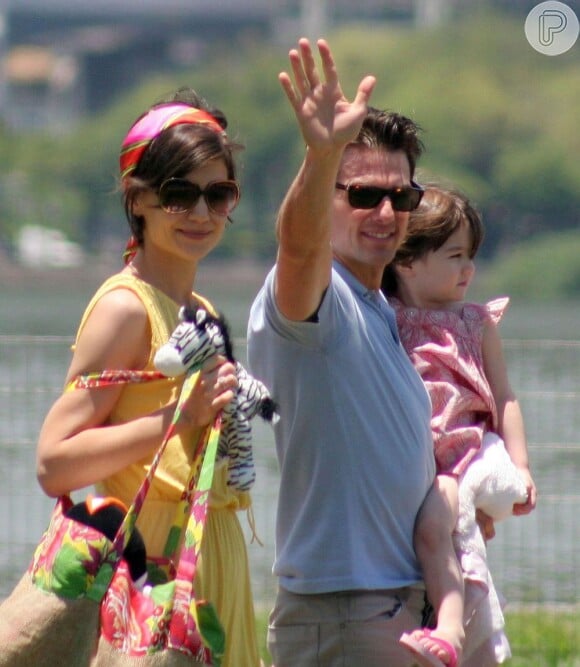 Tom Cruise acena para fotógrafo enquanto leva a filha, Suri, para passear durante visita ao Brasil. Katie Holmes carrega os brinquedos da menina, em fevereiro de 2009