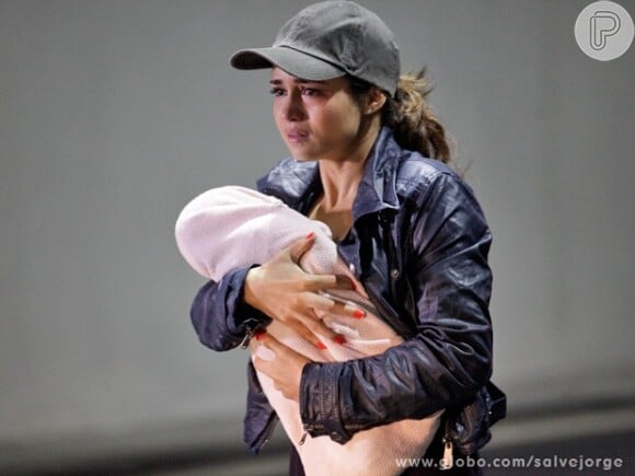 Morena (Nanda Costa) sai de um carro blindado carregando sua filha ainda bebê, em meio a um tiroteio, em 'Salve Jorge'