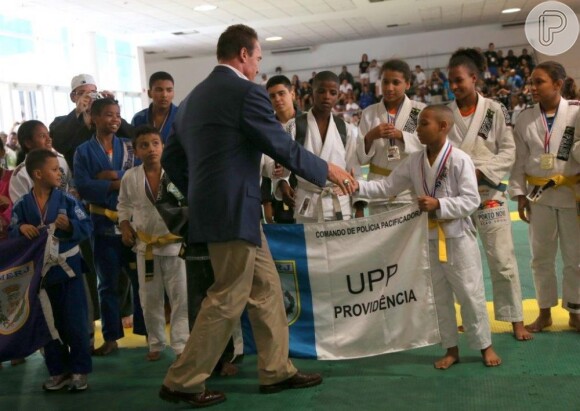 Arnold Schwarzenegger aperta a mão do jovem atleta