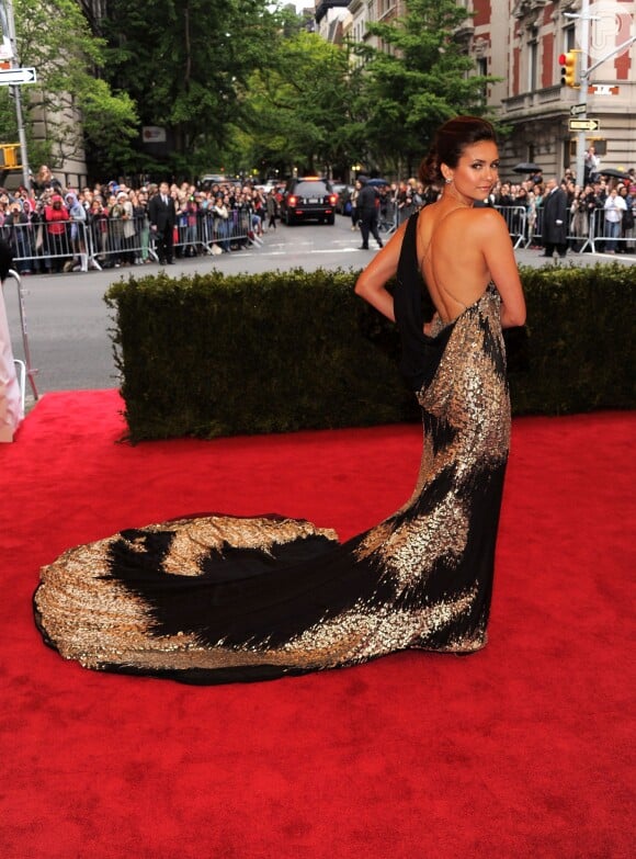 Em 2012, Nina Dobrev deixos as costas de fora em um vestido preto e dourado de cauda longa, no Met Gala