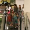 Cláudia Abreu segura as mãos dos filhos na escada rolante do shopping
