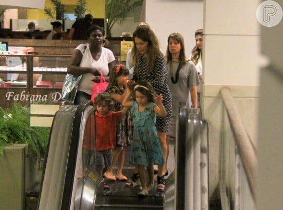 Cláudia Abreu segura as mãos dos filhos na escada rolante do shopping