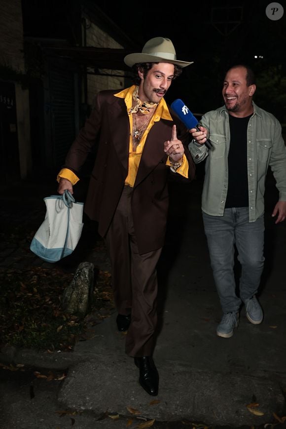 Chay Suede: com o charme caricato de Senhorzinho Malta (Roque Santeiro), Chay vestiu um terno marrom elegante sobre uma camisa amarela viva de gola aberta e um lenço estampado no pescoço. O visual é finalizado com o icônico chapéu de aba larga, bigode marcante e uma sobreposição de relógios e pulseiras douradas no pulso