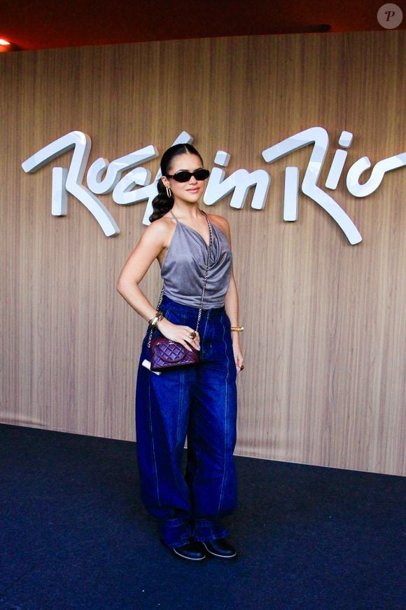 Maisa optou por um top de frentes únicas em tom cinza-chumbo com caimento fluido e decote degagê. A peça principal é combinada com uma calça jeans wide leg de lavagem escura e cintura alta, complementada por bolsa tiracolo vinho em matelassê da Chanel de R$ 30 mil, botas pretas de bico fino, óculos escuros estilo cat-eye e acessórios dourados nos pulsos