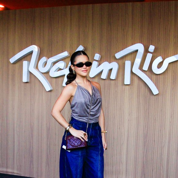 Maisa optou por um top de frentes únicas em tom cinza-chumbo com caimento fluido e decote degagê. A peça principal é combinada com uma calça jeans wide leg de lavagem escura e cintura alta, complementada por bolsa tiracolo vinho em matelassê da Chanel de R$ 30 mil, botas pretas de bico fino, óculos escuros estilo cat-eye e acessórios dourados nos pulsos