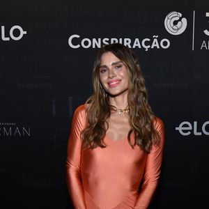 Carolina Dieckmmann apostou em um look salmão e uma bolsa prateada, sorrindo para os fotógrafos do local