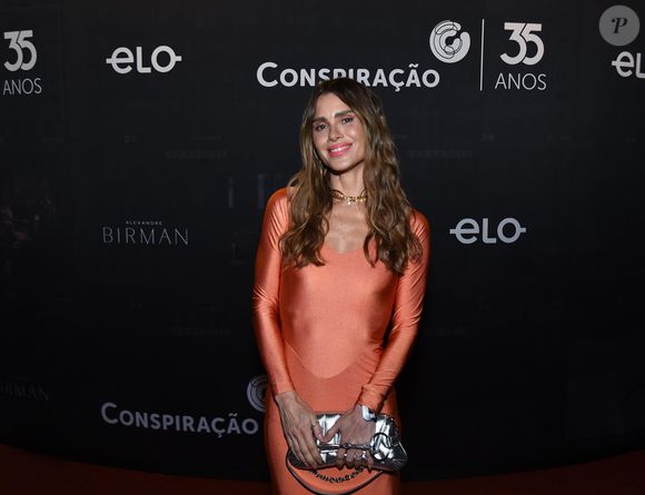 Carolina Dieckmmann apostou em um look salmão e uma bolsa prateada, sorrindo para os fotógrafos do local