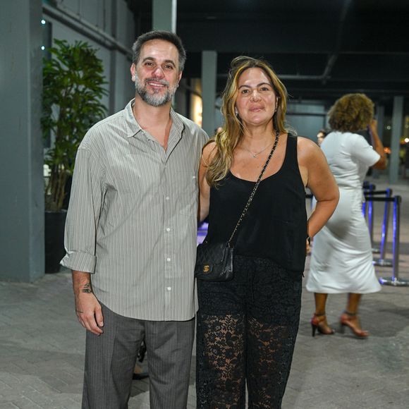 Carol Sampaio apostou no charme e transparência com uma regata preta básica combinada com uma calça pantalona de renda preta trabalhada. Ela complementou o visual com uma bolsa tiracolo de matelassê preta da Chanel. Ao seu lado, seu marido vestia uma camisa de listras finas com mangas dobradas, calça cinza de alfaiataria e tênis casuais em tons neutros