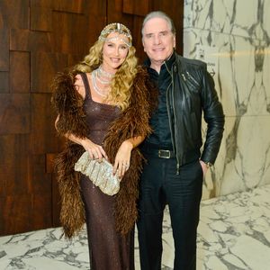 O empresário Roberto Justus e a influenciadora Ana Paula Siebert posaram juntos exibindo produções sofisticadas e repletas de textura: enquanto ele optou por um visual all black alinhado, combinando camisa social, calça de alfaiataria e uma jaqueta de couro utilitária com zíperes aparentes, ela roubou a cena com um longo vestido marrom em malha de brilho translúcida, complementado por uma imponente estola de plumas felpudas, sandálias de tiras finas e uma luxuosa headpiece cravejada de cristais que descia em camadas pelo colo