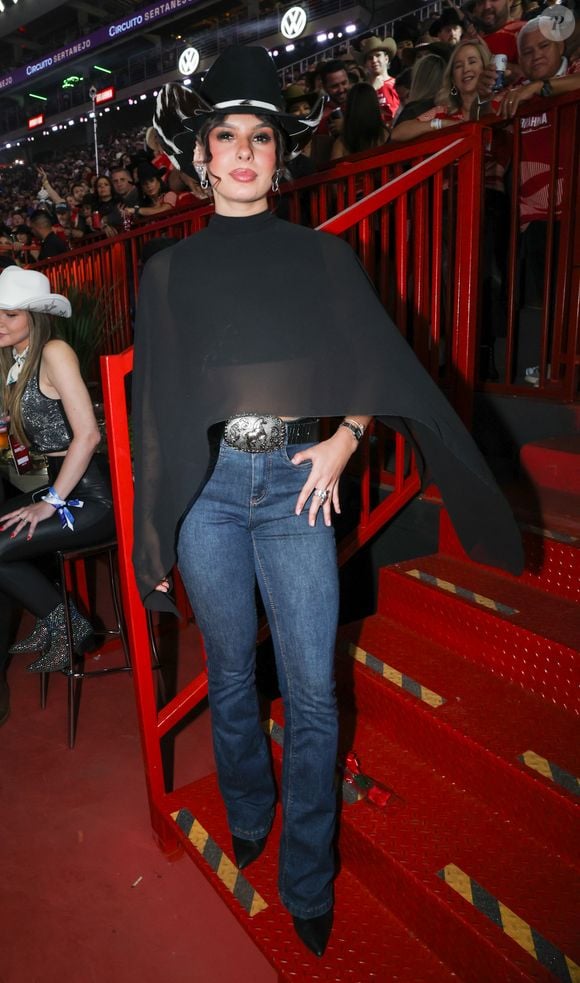 Ana Castela escolheu um look country sofisticado com chapéu estilizado, capa preta fluida, jeans justo e bota de bico fino