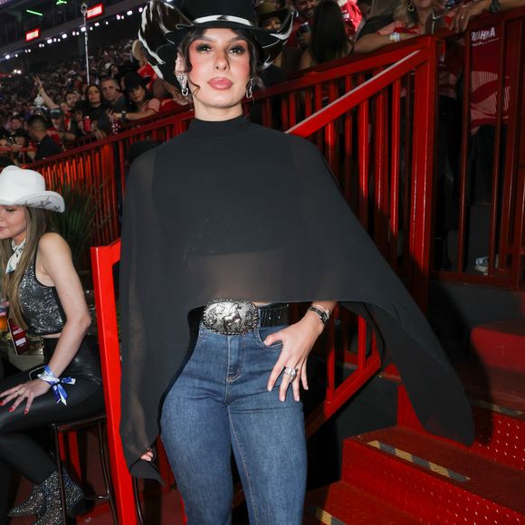 Ana Castela escolheu um look country sofisticado com chapéu estilizado, capa preta fluida, jeans justo e bota de bico fino