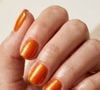 Para quem quer fugir dos tons discretos, o laranja dopamina é uma aposta certeira para a primavera. A versão brilhante e metalizada transforma as unhas curtas em protagonistas do look