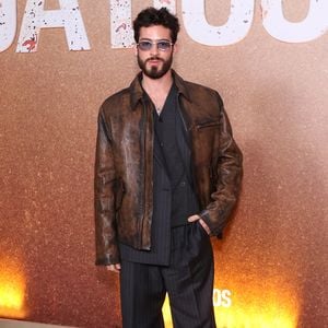 João Guilherme aposta na estética over-layered ao sobrepor uma jaqueta de couro marrom envelhecido a um terno risca-de-giz cinza-chumbo de proporções amplas. O look ganha ares urbanos com calça pantalona fluida, sapatos de bico fino e óculos de sol com lentes translúcidas azuladas