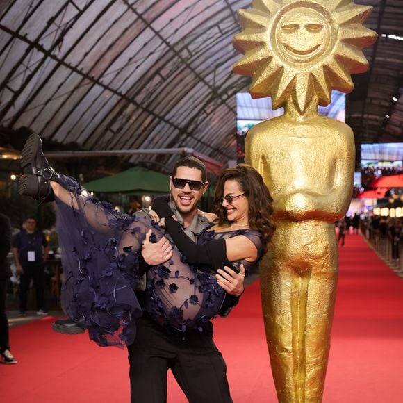Fernanda Marques e José Loreto chamaram atenção no tapete vermelho de Gramado com beijo e looks contrastantes: ela apostou em transparência e flores 3D; ele, em alfaiataria cinza e preta