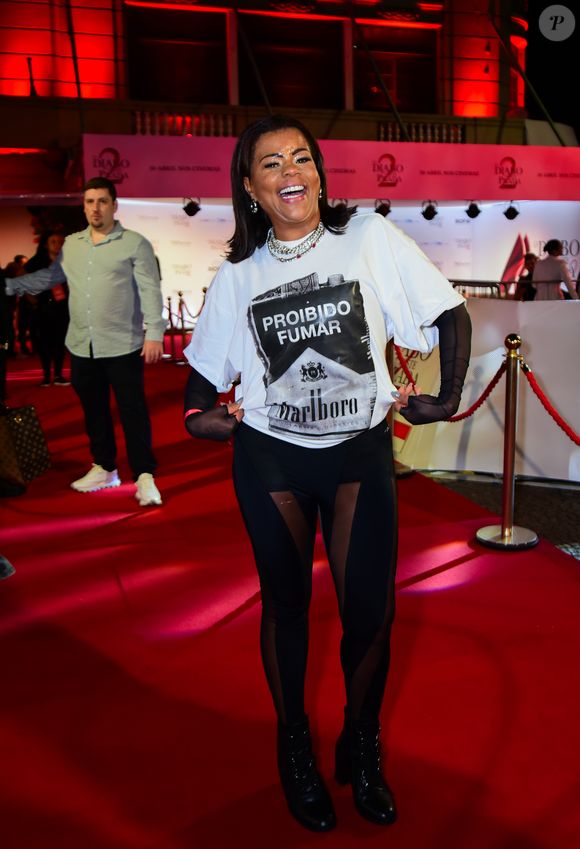 Tati Quebra Barraco trouxe a irreverência do Rio para o tapete. A funkeira ousou e utilizou uma camiseta oversized branca com uma estampa frontal provocativa que simula um maço de cigarros com o aviso 'Proibido Fumar'. Para elevar o visual ao contexto de gala, ela combinou a peça com luvas de tule pretas que se estendem até os ombros e uma calça legging com recortes em transparência, finalizando com botas de salto tratorado e colares de corrente prateada.