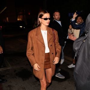A versatilidade do mule aparece também nas inspirações de moda de Hailey Bieber, que aposta em uma produção de streetwear oversized de luxo com sobretudo de camurça marrom-terroso, blusa branca de gola alta e minissaia de couro marrom