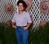 'Tia' Milena: apresentou uma proposta casual e despojada ao combinar uma camisa social de mangas curtas com estampa de listras verticais finas em roxo e branco, usada por dentro da calça. A composição incluiu uma calça jeans azul de lavagem média, cinto fino preto e sandálias de salto blocado marrons