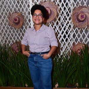 'Tia' Milena: apresentou uma proposta casual e despojada ao combinar uma camisa social de mangas curtas com estampa de listras verticais finas em roxo e branco, usada por dentro da calça. A composição incluiu uma calça jeans azul de lavagem média, cinto fino preto e sandálias de salto blocado marrons