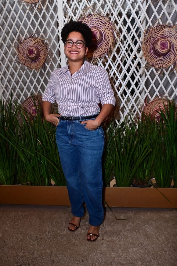 'Tia' Milena: apresentou uma proposta casual e despojada ao combinar uma camisa social de mangas curtas com estampa de listras verticais finas em roxo e branco, usada por dentro da calça. A composição incluiu uma calça jeans azul de lavagem média, cinto fino preto e sandálias de salto blocado marrons
