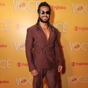 Amaury Lorenzo investe na elegância contemporânea com terno monocromático em tom marrom-feijão, composto por paletó envelope com amarração lateral em faixa e calça reta de caimento fluido. Nos acessórios, destaca-se o uso de óculos escuros e sapatos sociais escuros