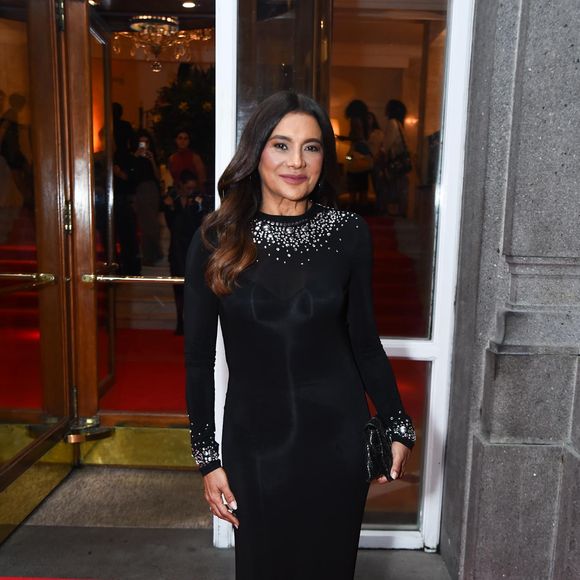 Dira Paes escolheu um vestido preto de mangas longas e gola alta, cuja sobriedade é quebrada por um trabalho primoroso de pedrarias no decote e nos punhos. Os cristais prateados e fumê formam uma espécie de colar integrado à peça, trazendo luz direta para o rosto. O corte reto do vestido garante uma silhueta alongada e atemporal