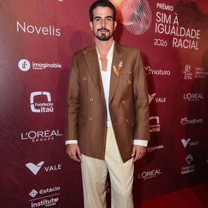 Enzo Celulari exibiu uma produção sofisticada em tons terrosos, composta por um blazer de abotoamento duplo (double-breasted) em marrom chocolate com botões dourados. Ele combinou a peça estruturada com uma calça de alfaiataria em tom creme de caimento impecável e uma regata branca básica por baixo