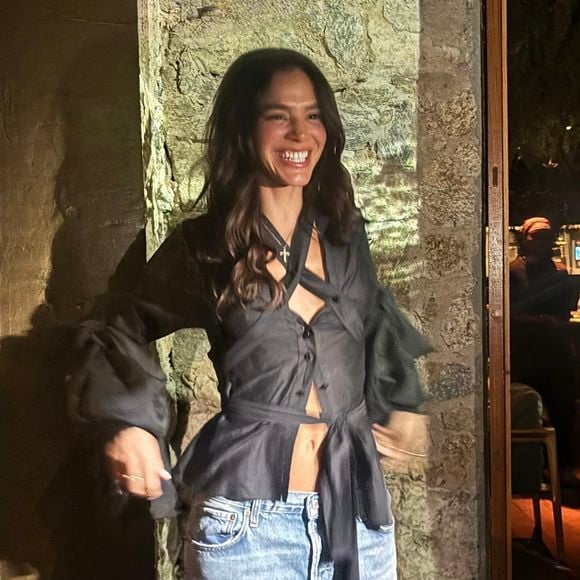 Bruna Marquezine exibiu uma blusa preta de amarração, que traz decote profundo com recortes e destaca a barriga sarada