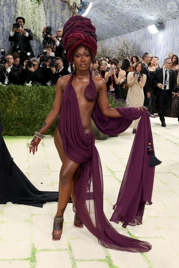 UAU! Doechii entrega tudo no Met Gala 2026 com um look bordô profundo, ousadíssimo, que remete a estátuas pelo drapeado. O visual ganha ainda mais impacto com um turbante opulento - e detalhe: descalça