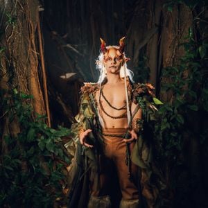 João Victor Gonçalves, o Mau Mau de 'Quem Ama Cuida' apostou em um look todo inspirado no deus Pã: o look é composto por uma capa em camadas de tecidos fluídos e esfarrapados em tons de verde-oliva e marrom, decorada com folhagens nos ombros. O peitoral fica à mostra, adornado por cordões trançados em tom terroso, acompanhado por calça justa marrom com cinto trançado e polainas felpudas de pele sintética nos pés. Nos braços, ostenta braçadeiras estruturadas com detalhes folhosos. O destaque fica para a caracterização facial, que inclui próteses de chifres avermelhados, orelhas pontudas, maquiagem artística facial e longas mechas brancas