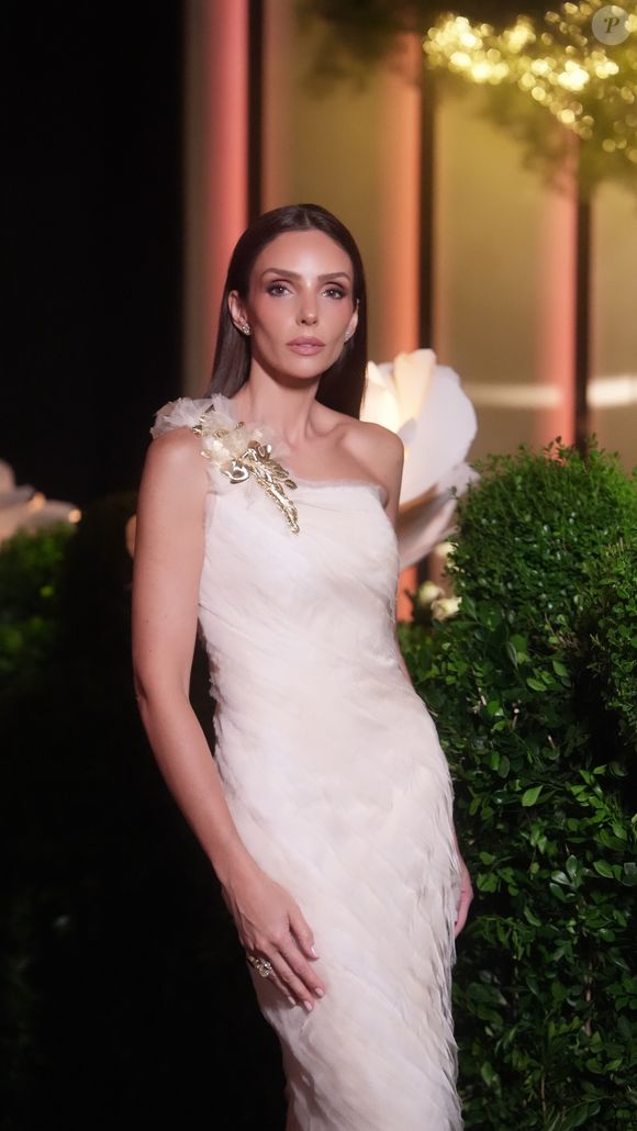 Mãe da debutante, Carol Celico apostou em um vestido branco de tecido leve e texturizado, destacado pela aplicação floral dourada no ombro