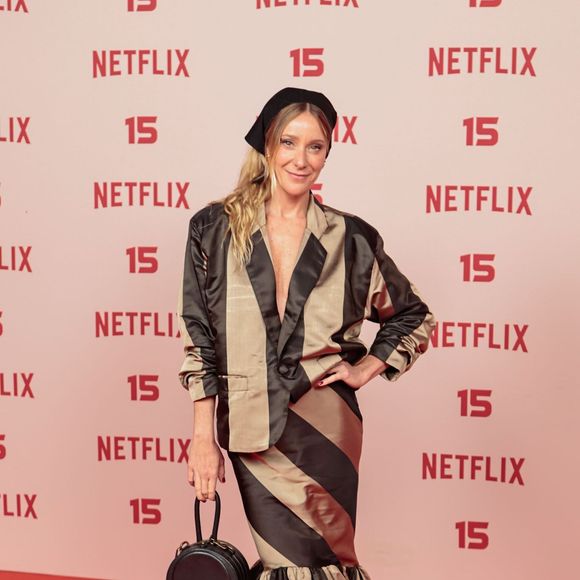 Carol Abras: usa um conjunto estampado com listras largas diagonais em bege e preto, composto por blazer estruturado decotado e saia longa ajustada com barra armada em babados, combinados com faixa de cabelo e bolsa redonda preta