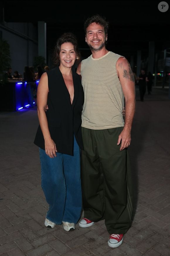 Fabíula Nascimento apostou em uma alfaiataria descontraída com um colete preto decotado sem mangas, jeans wide leg e tênis claros. Ao seu lado, Emílio Dantas combinou uma regata regata listrada em tom bege com calça oversized verde-militar e tênis All Star vermelho de cano baixo. O casal exibiu um visual urbano, moderno e cheio de personalidade
