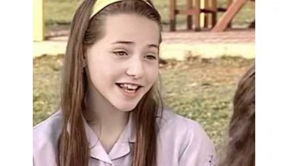 Letícia Colin aparece ainda jovem com cabelo longo e castanho, usado em uma base reta e com poucos elementos de camadas. O visual mantém os fios compridos e naturais, com uma discreta moldura ao redor do rosto