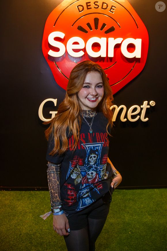 Klara Castanho escolheu uma produção rockstar com camiseta do Guns N' Roses, blusa de animal print por baixo, short preto, meia-calça e acessórios prateados