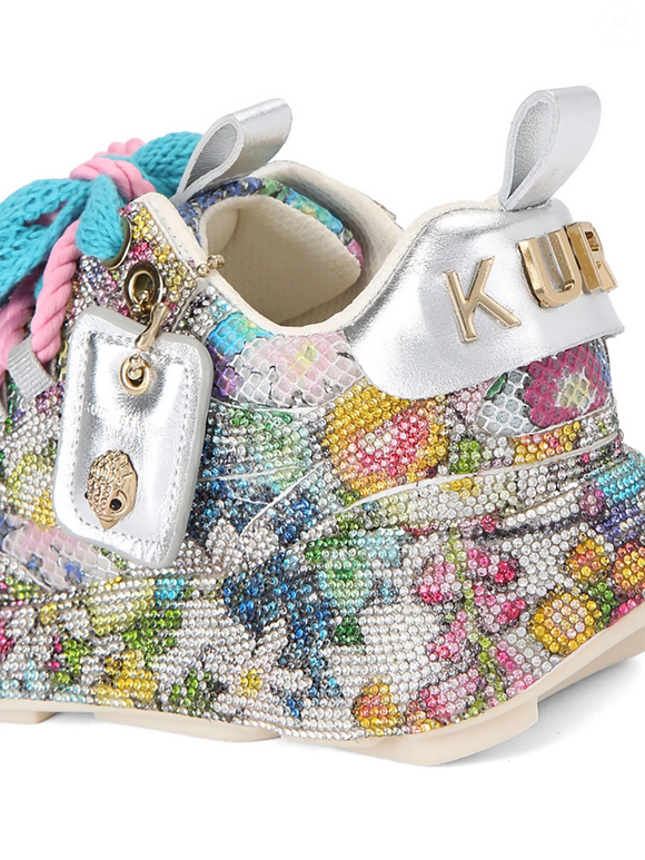 O tênis da Kurt Geiger London combina estampa floral, paetês, cadarços trançados em azul e rosa e solado chunky, criando uma proposta nada discreta