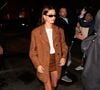 A versatilidade do mule aparece também nas inspirações de moda de Hailey Bieber, que aposta em uma produção de streetwear oversized de luxo com sobretudo de camurça marrom-terroso, blusa branca de gola alta e minissaia de couro marrom