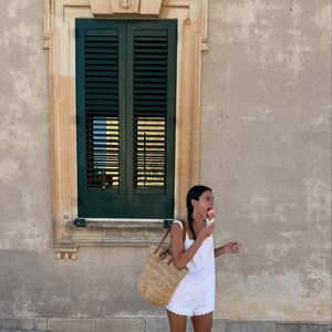 Bruna Marquezine combina macaquinho branco com detalhes em renda com bolsa grande de palha e par de Havaianas