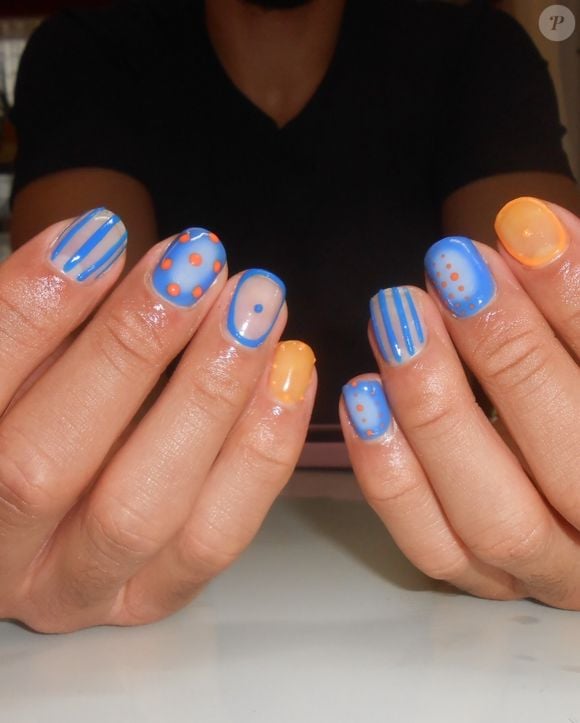 O Airbrush & Transparência traz uma referência diretamente ligada à estética Y2K. A proposta mistura esmaltes azul e laranja com efeito degradê e aerógrafo, além de transparências, poás e listras finas. O visual fica moderno pela combinação de elementos delicados e detalhes gráficos