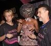 De vestido míni, Adriane Galisteu elegeu acessório inusitado para cabeça e precisou da ajuda do marido, Alexandre Iódice, e do filho, Vittorio, se locomover