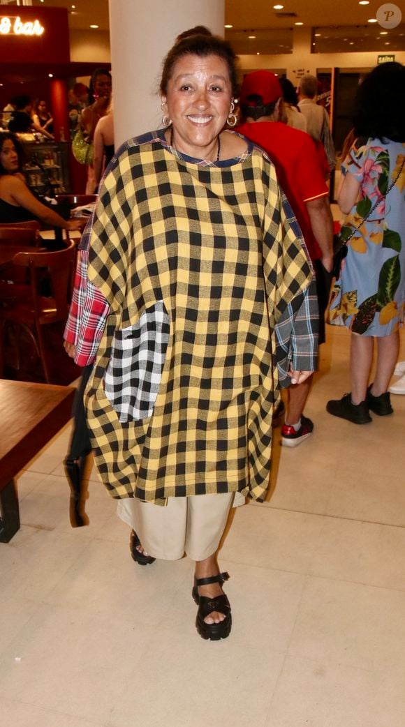 Regina Casé usou uma blusa oversized de estampa xadrez em amarelo, preto e branco, combinada a uma calça bege e sandálias pretas de plataforma