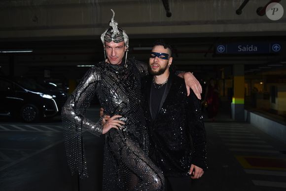 Dudu Bertholini ousou em um look futurista repleto de cristais e aplicações metálicas, acompanhado de adereço de cabeça escultural, enquanto o parceiro seguiu no clássico preto com toques de brilho